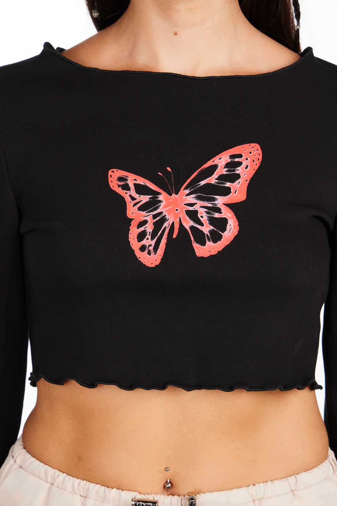 A person is wearing the "Butterfly Long Sleeve Crop" by Sunshine Rollers, featuring a red butterfly design on the front. The black crop top has a wavy, raw hemline, and the person's navel is adorned with a silver ring.