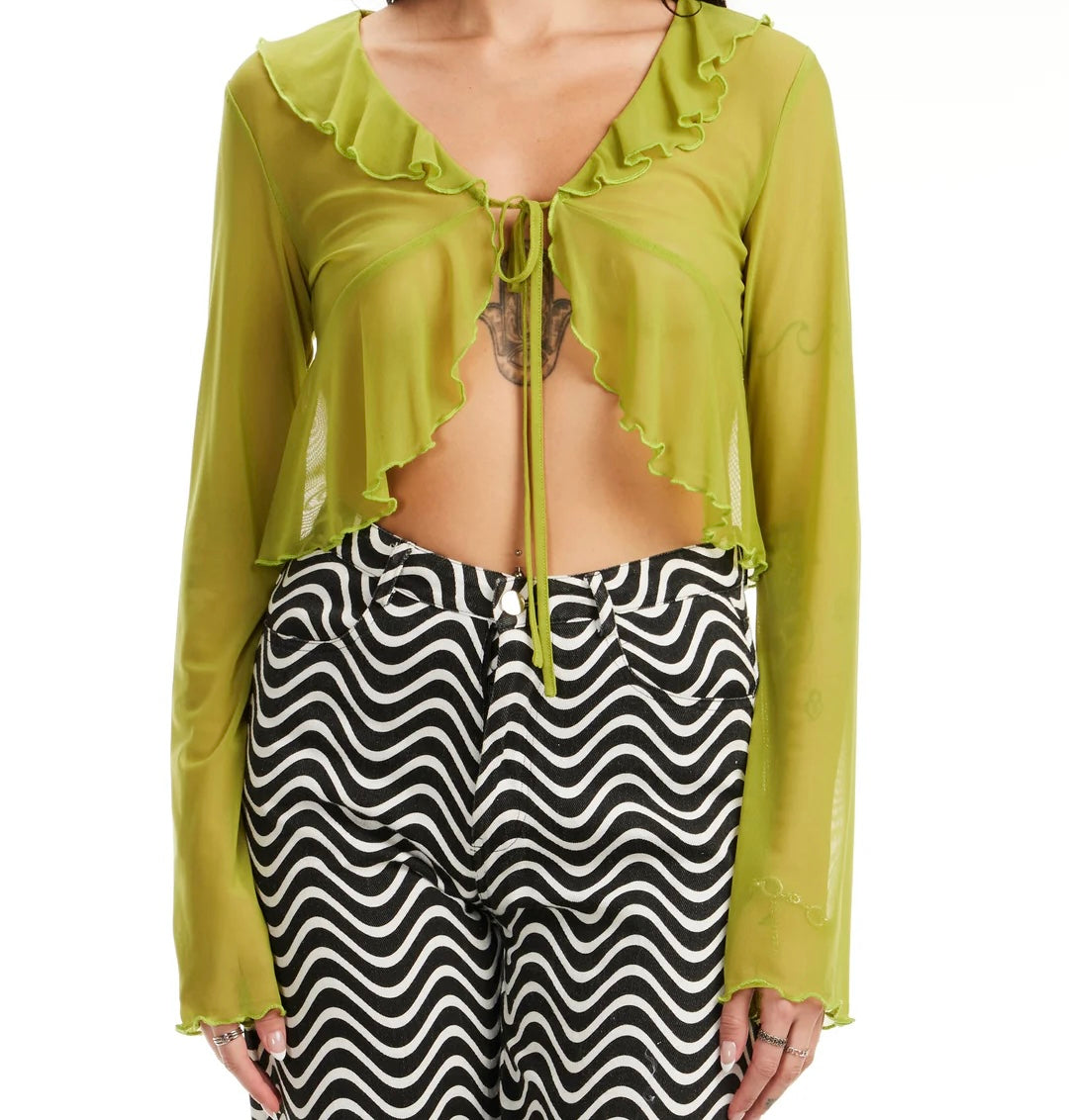 A person is wearing the Mesh Tie Front Crop Long Sleeved top by Sunshine Rollers in lime green, paired with black and white wavy-patterned pants. Their midriff is visible, showcasing a tattoo on their chest.